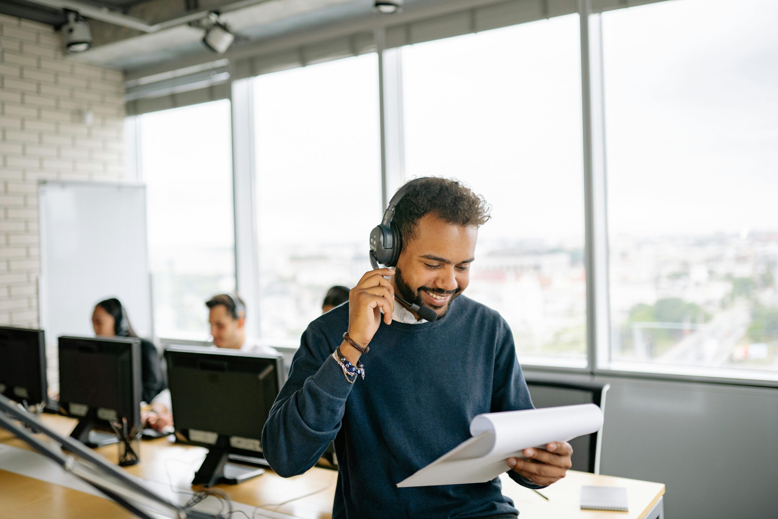 Friendly call center agent engaged in conversation while reviewing documents at his desk.